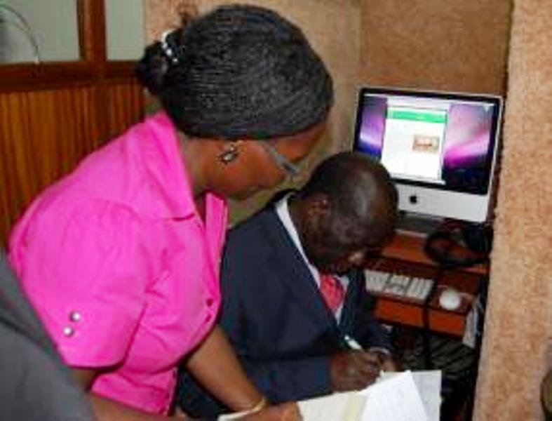 H.E. Edward Kiwanuka Ssekandi (R) assisted by Dr. Sylvia Nannyonga-Tamusuza (L) signs the Visitors' Book in the Music Archive.