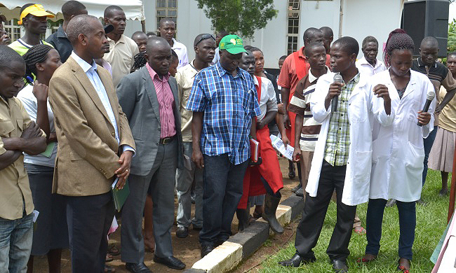 NAADS ED-Dr. Samuel Mugasi (2nd L) listens to a presentation by Students on African Swine fever accompanied by Dr. Denis Mpairwe (In cap-4th L) and Student Representative Mr. Isabirye Hamidu (3rd L) during the 1st Yr Internship Exhibition on 8h August 2014, MUARIK, CAES, Makerere University, Wakiso, Uganda