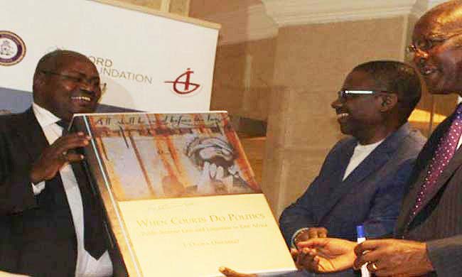 Chief Justice-Hon. Justice Bart Katureebe (R) assisted by Principal Judge-Dr. Yorokamu Bamwine (L) and Prof. Oloka Onyango (C) signs a dummy of "When Courts Do Politics" during the book launch, 12th April 2018, Pearl of Africa Hotel, Kampala Uganda