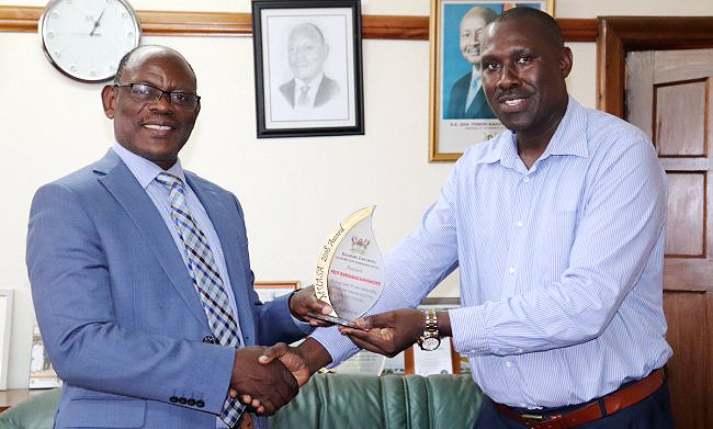 The Vice Chancellor, Prof. Barnabas Nawangwe (L) receives his award as as the outstanding personality supporting MUASA activities from the Chair Welfare-MUASA Mr. Arthur Mugisha (R) on 17th December 2018 in his Office, Main Building, Makerere University, Kampala Uganda