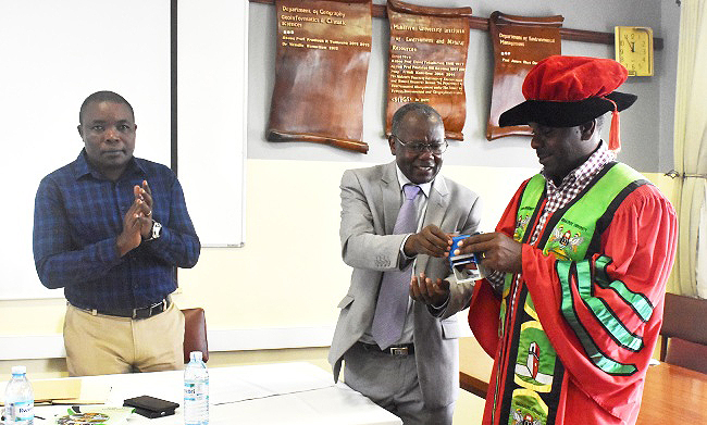The Principal CAES-Prof. Bernard Bashaasha (C) hands over the Instruments of Power to Incoming Dean SFEGS-Assoc. Prof. Fred Babweteera (R) as Outgoing Dean SFEGS-Prof. Mnason Tweheyo (L) applauds on 11th January 2019, Makerere University, Kampala Uganda