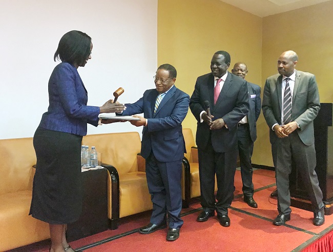 The New Chairperson of Council Mrs Lorna Magara receiving  Instruments of Power from the Chancellor Prof. Ezra Suruma. Other members presents is the Outgoing Chairperson of Council Eng.Dr. Charles Wana-Etyem and the University Secretary Mr. Charles Barugahare.