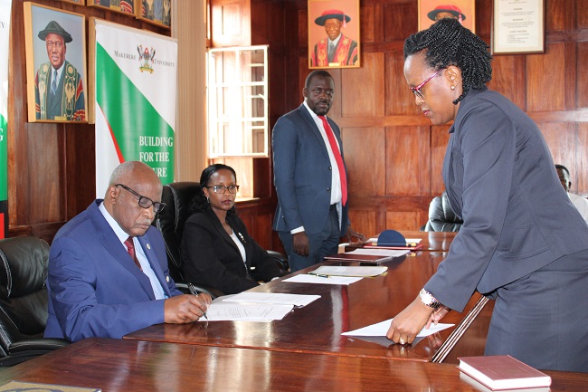 Justice John Patrick Mashongo Tabaro (L) witnesses the swearing in of Dr. Phiona Muhwezi-Mpanga (R). Second Left is the Chairperson of Council Mrs. Lorna Magara and Acting University Secretary Mr. Yusuf Kiranda (3rd L).