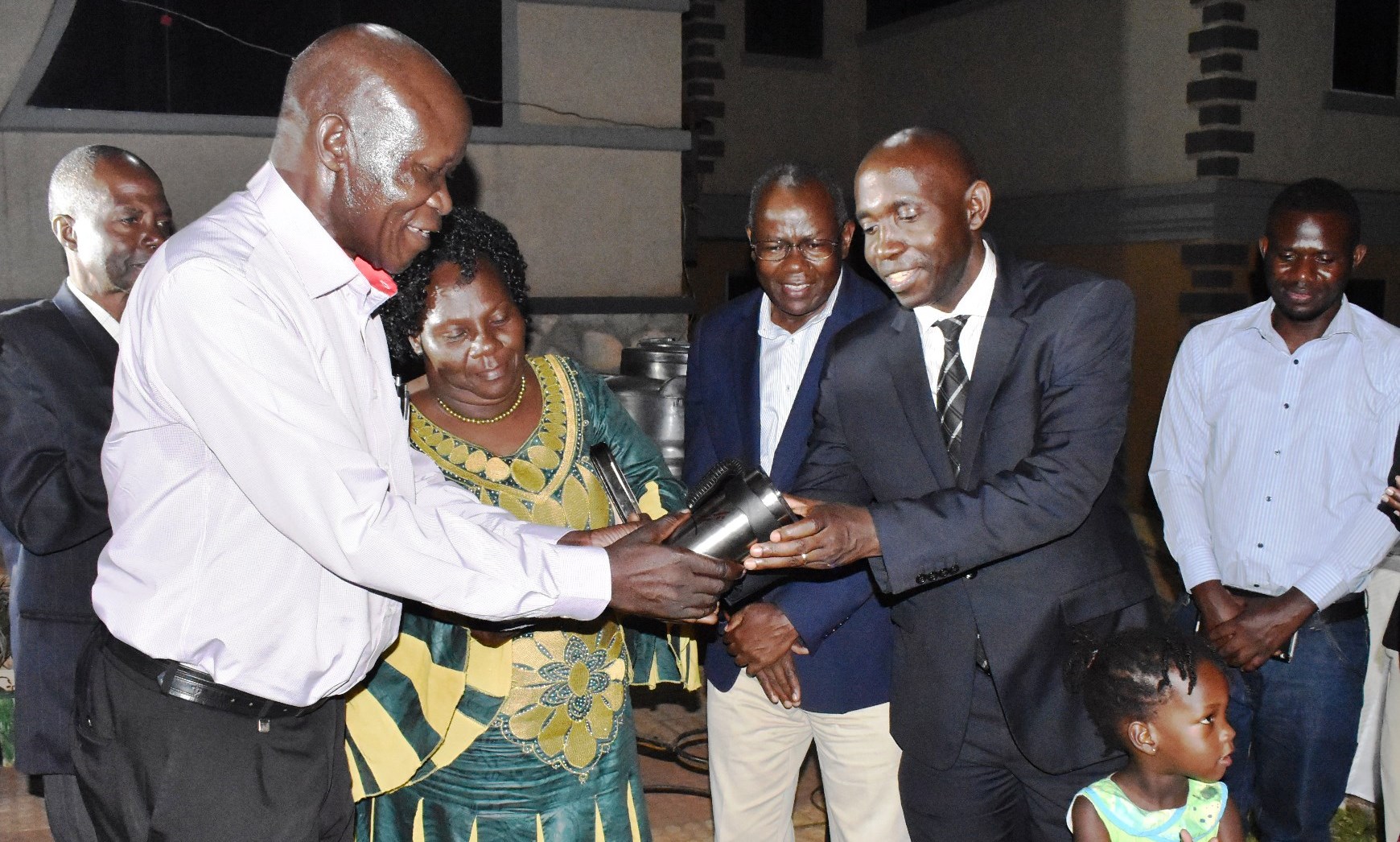 Dr. John Steven Tenywa (Left) flanked by his wife receives a coffee mug from the new Head, Department of Agricultural Production (DAP) and former Mentee Dr. J. B. Tumuhairwe, as Principal CAES-Prof. Bernard Bashaasha (Rear Blue Jacket) witnesses during the function on 17th August 2019, Grand Global Hotel, Kampala Uganda