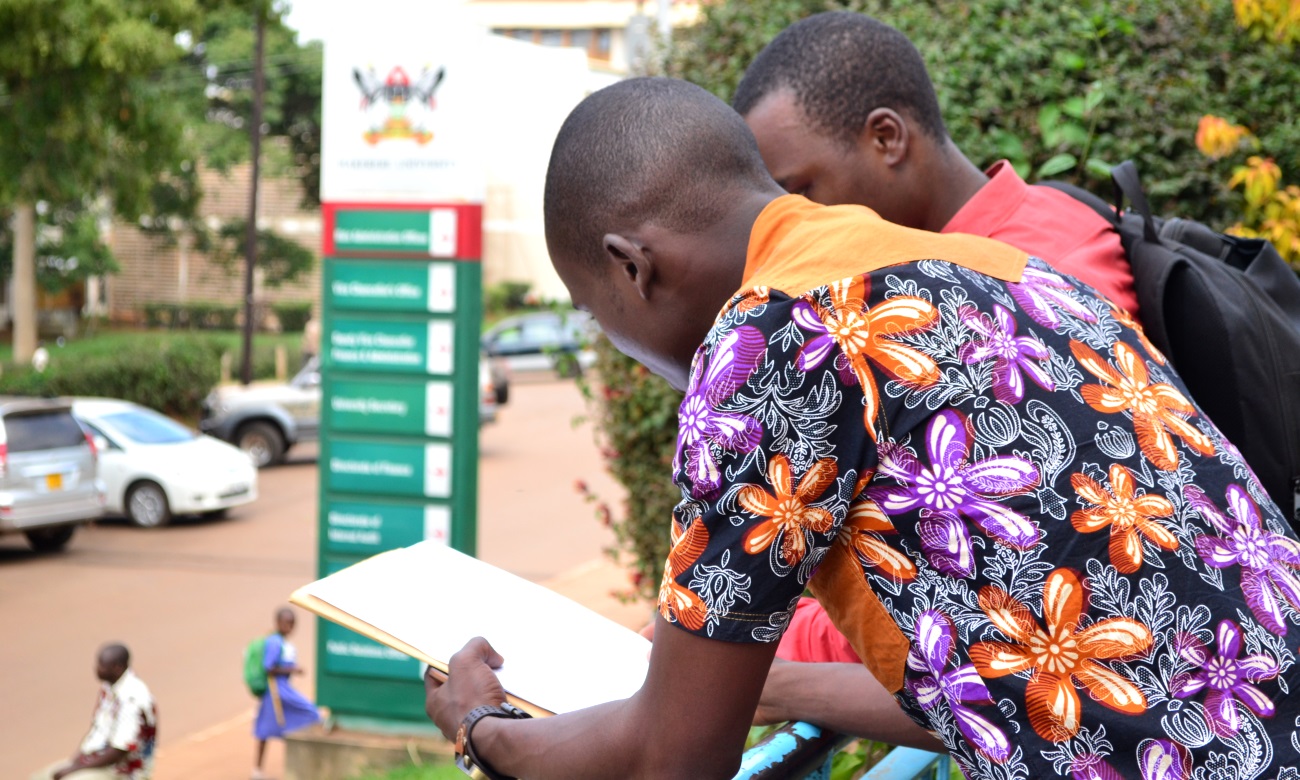 Male students lean on the rail overlooking University Road at the Main Building, Makerere University, Kampala Uganda.