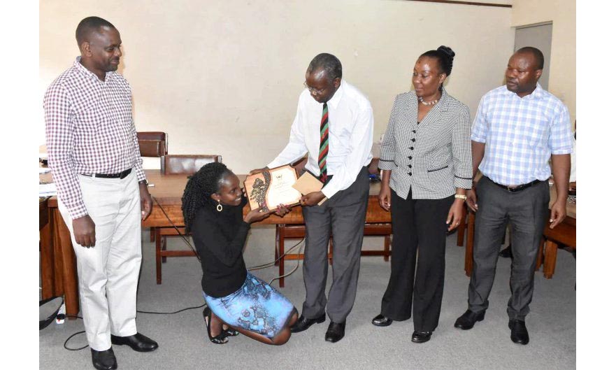 Ms. Sarah Namayengo (Kneeling) receives the plaque and cash reward from the Principal CAES-Prof. Bernard Bashaasha (Centre) flanked by L-R: Dr. Fred Babweteera, Deputy Principal CAES-Dr. Gorettie Nabanoga and the Head FBT-Dr. Edward Nectar Mwavu during the College Academic Board Meeting, 27th February 2020, Conference Room, School of Agricultural Sciences, Makerere University, Kampala Uganda.