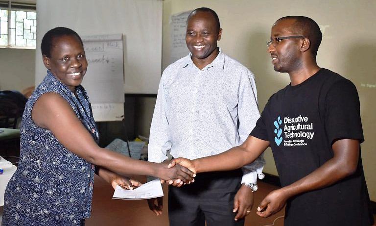 Apac District Agricultural Officer-Betty Okori (Left) receives her certificate of training from MAAIF Agronomist-Francis Nuwagira (Right) as Prof. Archileo Kaaya (Centre) who represented the Principal CAES at the closing ceremony witnesses on 6th March 2020, Continuing Agricultural Education Centre (CAEC), MUARIK, CAES, Wakiso Uganda.