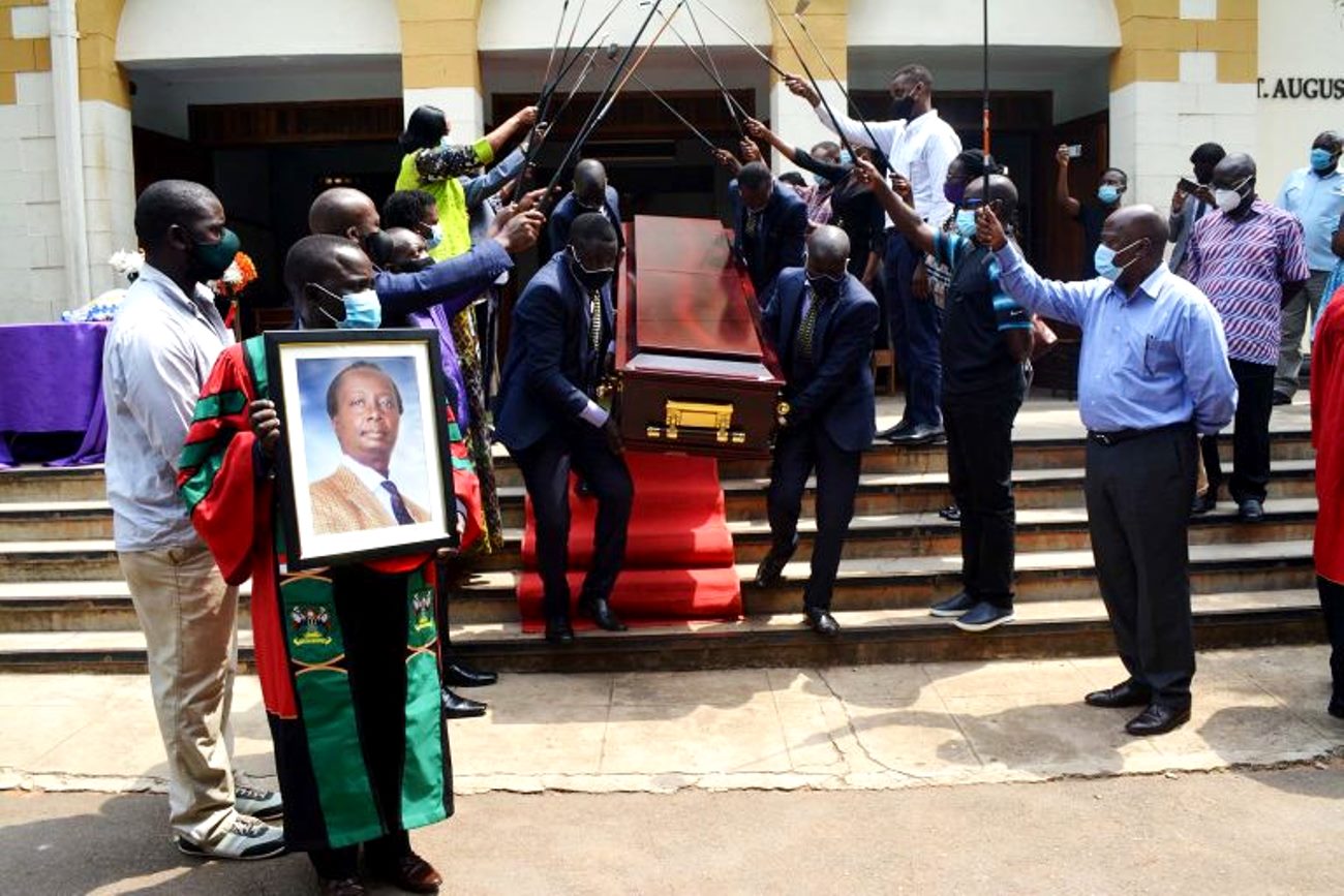 Chairperson MUASA-Dr. Deus Kamunyu Muhwezi bears the framed photo as pallbearers carry the late Prof. Anthony Kerali’s remains out of St. Augustine through an arch of clubs mounted by fellow golfers after the Requiem Mass on 23rd February 2021, St. Augustine Chapel, Makerere University.