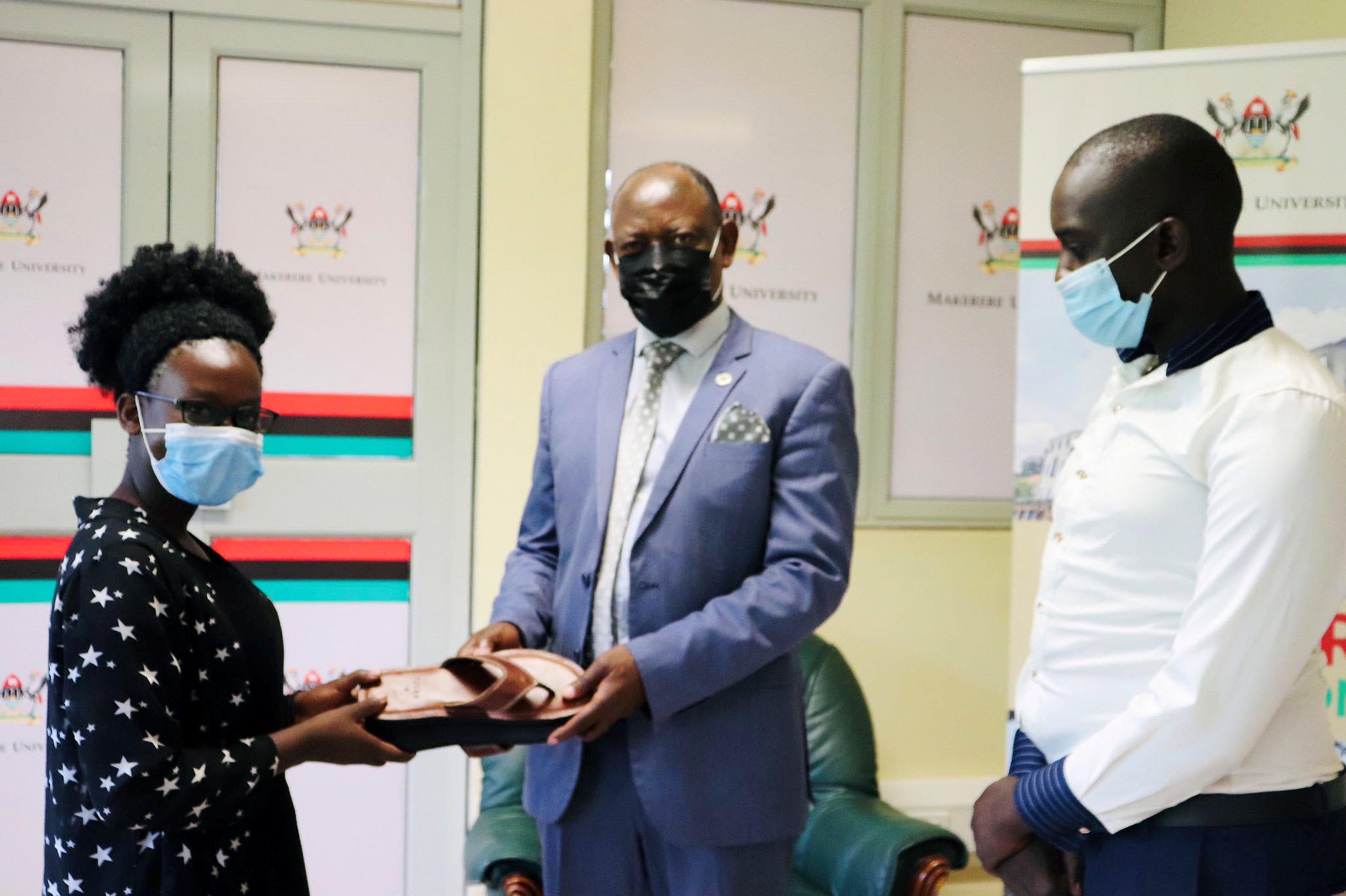 The Vice Chancellor, Prof. Barnabas Nawangwe (C) receives a pair of sandals from Miss Omega Mirembe (L) as Mr. Isaac Wanjala (R) witnesses on 28th April 2021, CTF1, Makerere University.