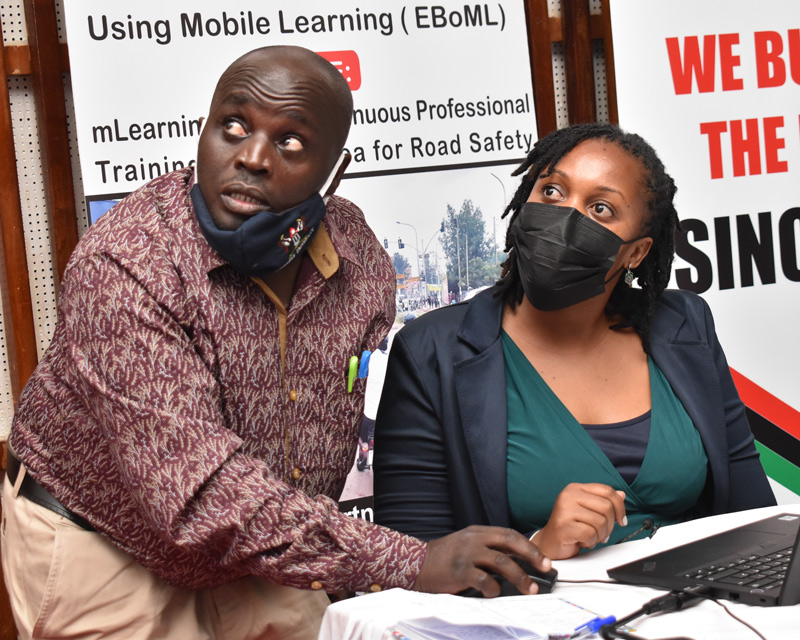 Ms. Lillian Mbabazi (R) assisted by the day's Emcee, Dr. Godfrey Mayende (L) makes her presentation on the Health and Safe-Living Module.