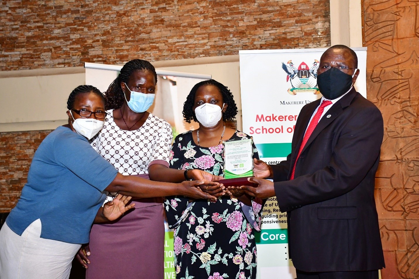 Dr. Maxwell Otim Onapa, the Director of Science, Research and Innovation at Ministry of Science, Technology and Innovation (R) hands over a plaque to Dr. Etheldreda Nakimuli (2nd R) and her team at SEEK-GSP project. Their project aimed at narrowing the treatment gap for depression among people living with HIV using group support psychotherapy delivered by community health workers. They are among the winners of the 2020 Social Innovations in Health Awards organized by the School of Public Health on 17th March 2021.