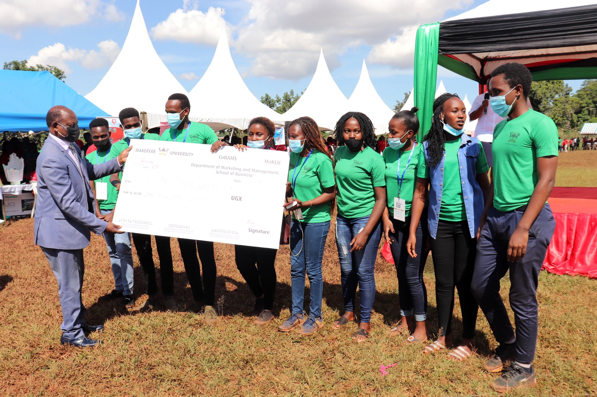 The Vice Chancellor, Prof. Barnabas Nawangwe (L) hands over a dummy cheque to the Spin Cycle Washing Machine Team at the end of the 5th Annual Entrepreneurship Students’ Expo on 5th May 2021, Rugby Grounds, Makerere University.