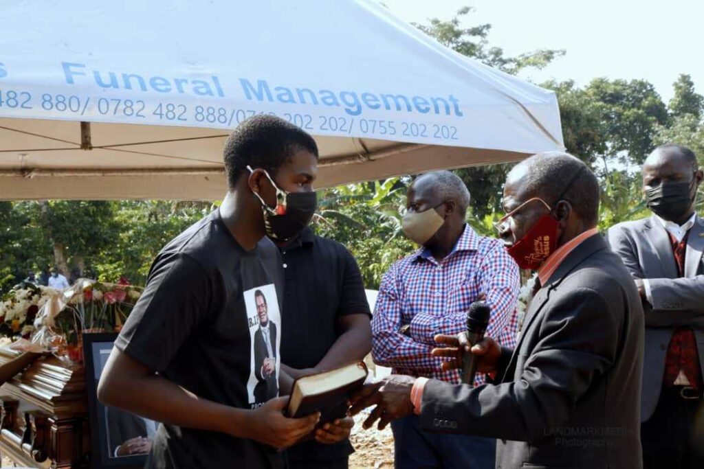 A member of the SDA clergy hands over a bible to one of Prof. Banadda's children