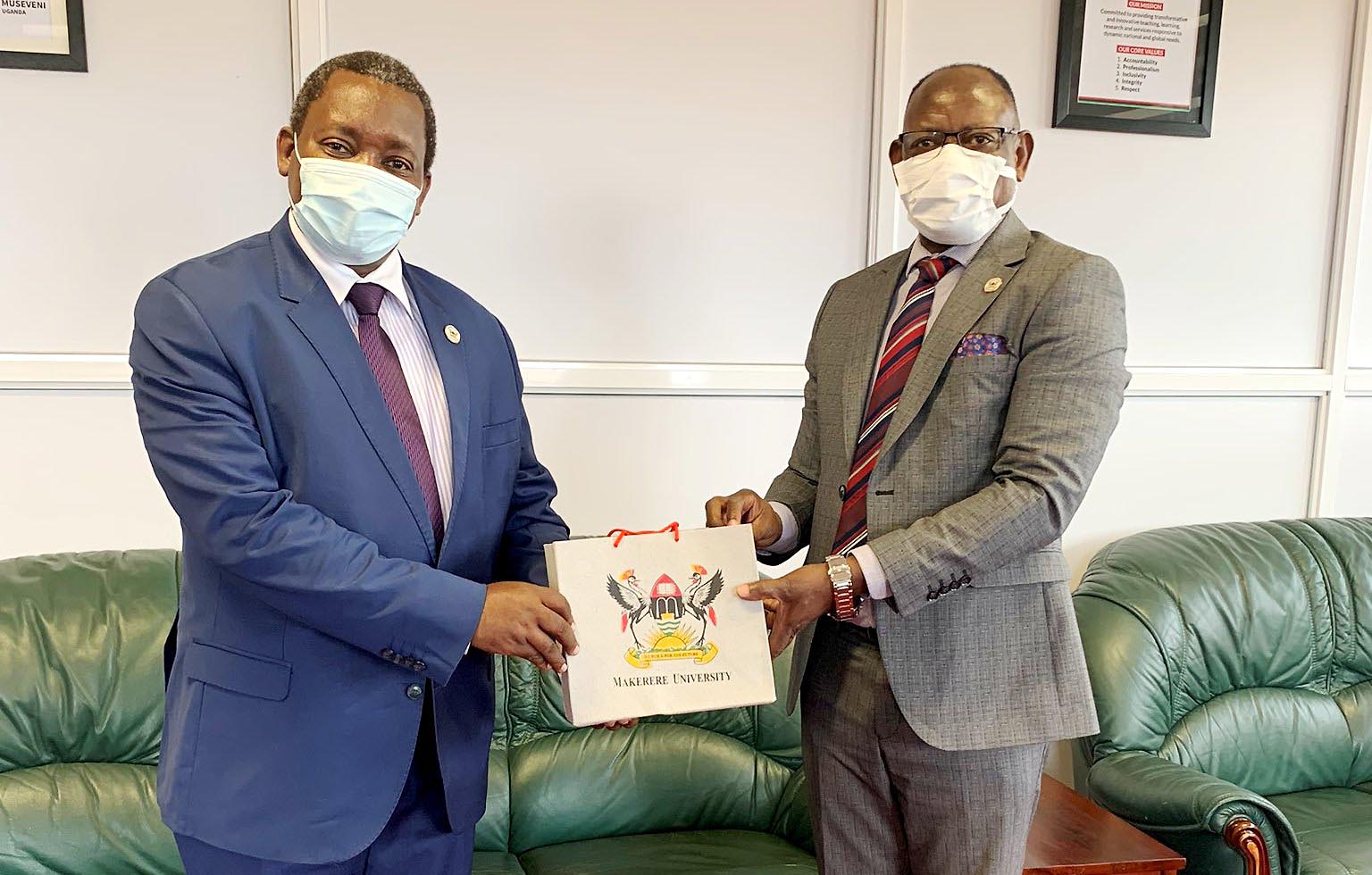 The Vice Chancellor, Prof. Barnabas Nawangwe (R) hands over an assortment of Mak souvenirs to ES IUCEA, Prof. Gaspard Banyakimbona (L) after their meeting on 24th August 2021, CTF1, Makerere University.