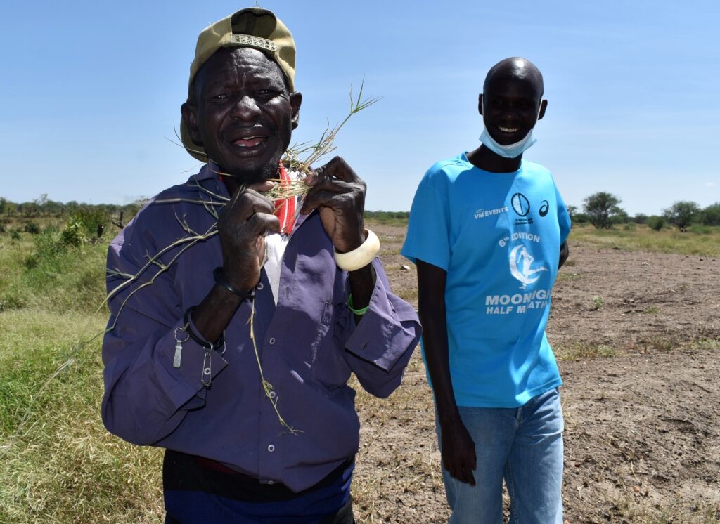 Clan elder Mr. Achok Lopeimal (L) demonstrates the importance of star grass during traditional marriage ceremonies as LC5 Chairman Mr. Loru Moses (R) listens attentively.