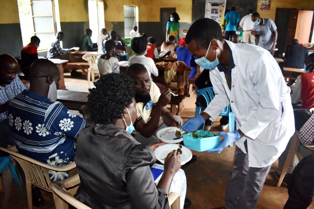 Undergraduate student Mr. Mwaka (white coat) serves some of the prepared soup to participants that gathered in the Kigorobya sub-County Community Hall, Hoima district. 