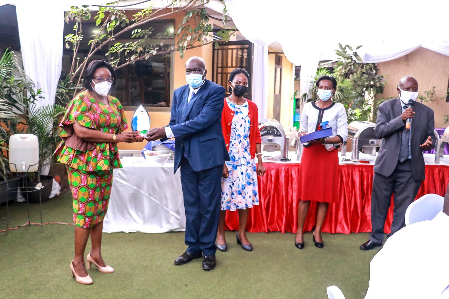 The Dean MakSPH-Prof. Rhoda Wanyenze (L) presents a plaque to Mr. Rudolf Buga (2nd L) as Dr. Esther Buregeya (C), Dr. John C. Ssempebwa (R) and another official witness during Mr. Buga's farewell ceremony held at Piato Restaurant in Kampala on 2nd December 2021.