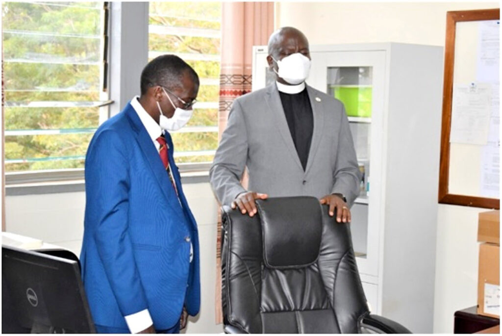 Rev. Onesimus Asiimwe (R) says a prayer of blessing over the incoming Principal’s seat.