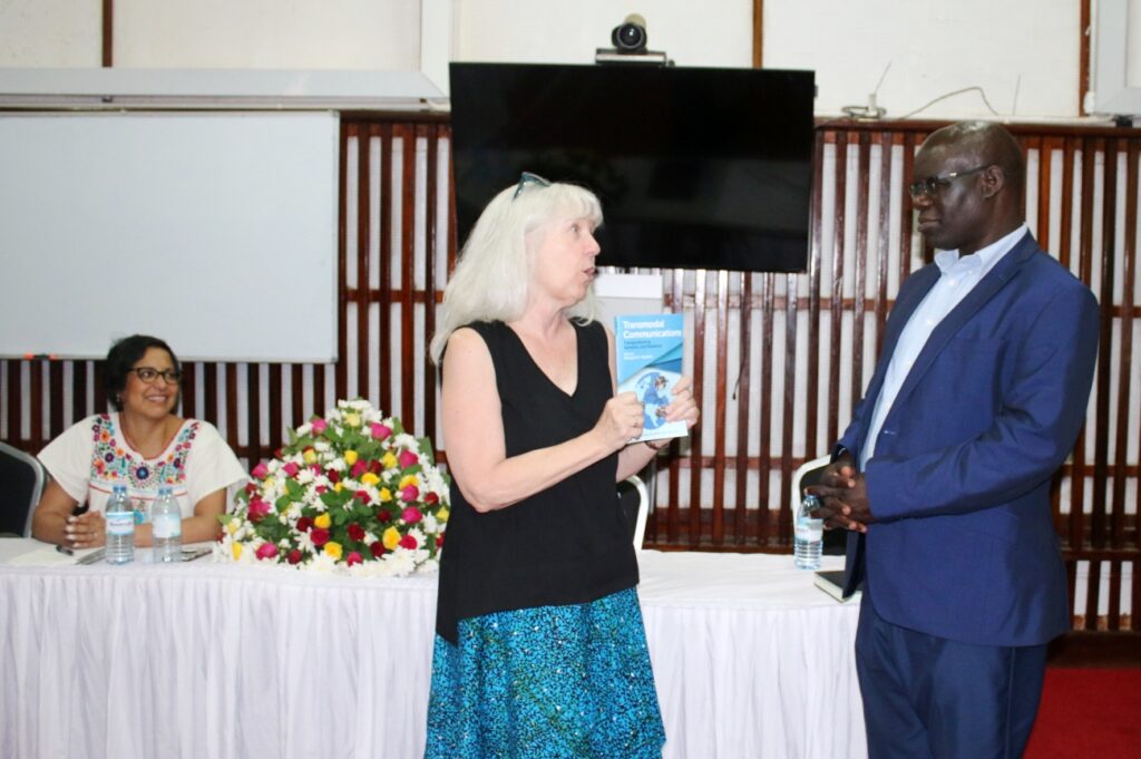 Prof. Maggie Hawkins (C) prepares to present a copy of the book "Transmodal Communications: Transpositioning Semiotics and Relations" to Dr. Willy Ngaka (L) as Dr. Mariana Castrol (L) witnesses. Dr. Ngaka contributed a chapter to the book. 