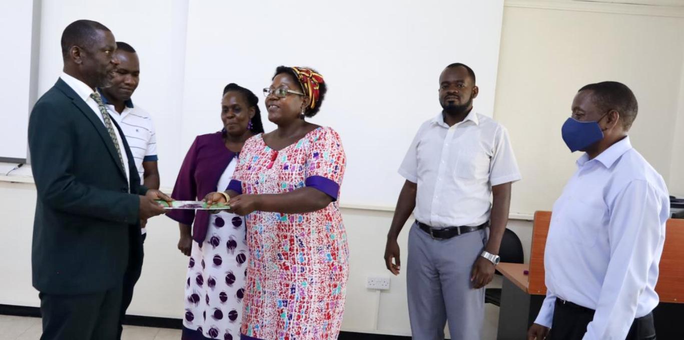 Assoc. Prof. Julius Kikooma (Left) hands over to the Principal Assoc. Prof. Josephine Ahikire (3rd Right) in the CHUSS Smart Room, Makerere University on 18th March 2022.