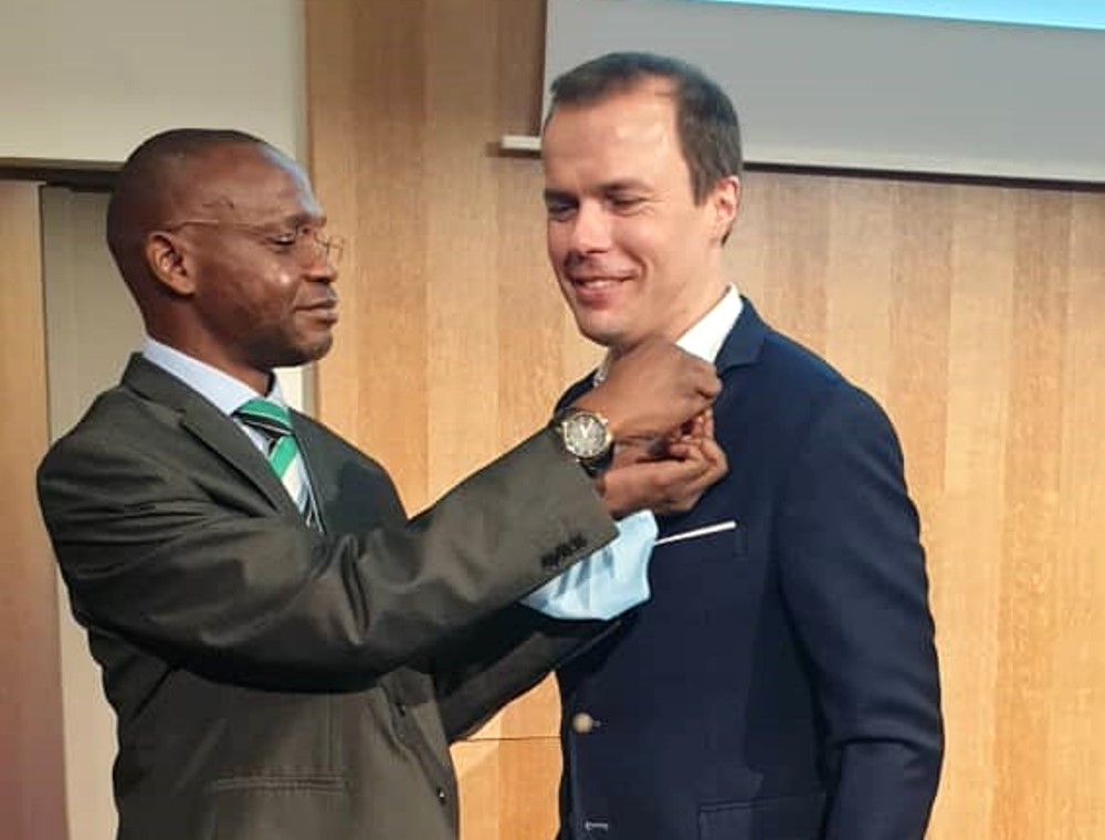 Associate Prof. Umar Kakumba (Left) decorates Dr. Christian Möllmann, Director of Strategic Partnerships, Université of Tubingen, Germany (Right) with a Makerere University lapel badge.