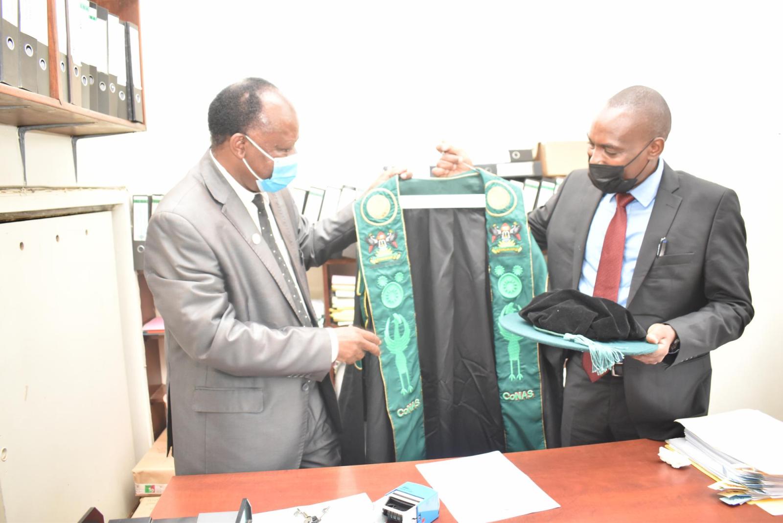 The outgoing Deputy Principal, CoNAS, Prof. Fredrick Jones Muyodi (L) hands over the ceremonial gown of the Deputy Principal CoNAS to the Principal, Dr Tumps Winston Ireeta during the ceremony on 7th March 2022.