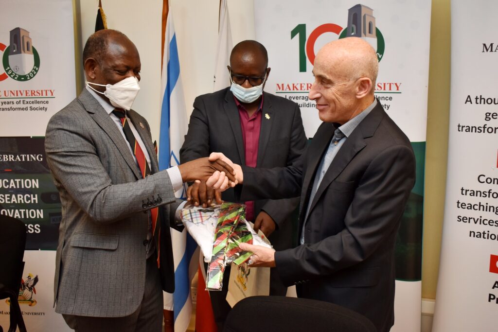 Prof. Barnabas Nawangwe (L) assisted by Mr. Agaba Issa Mugabo (C) presents an assortment of Makerere branded souvenirs to H.E. Michael Lotem (R) during the courtesy call. 