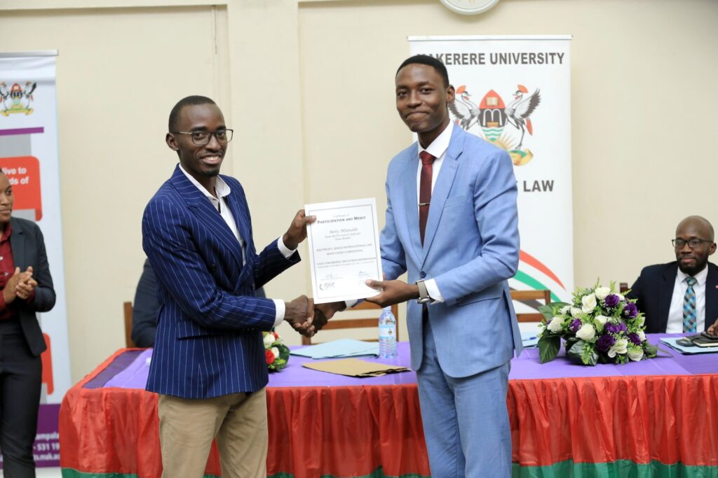 Benson Mayanja of Makerere University (Right) receives his Best Oralist of the 2022 Jessup National Rounds Award from President Philbert Kansiime (Left). Photo credit: Twitter/@MakMootSociety