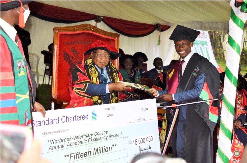Wafula Ivan receives a handshake from the Chancellor, inset is the dummy check