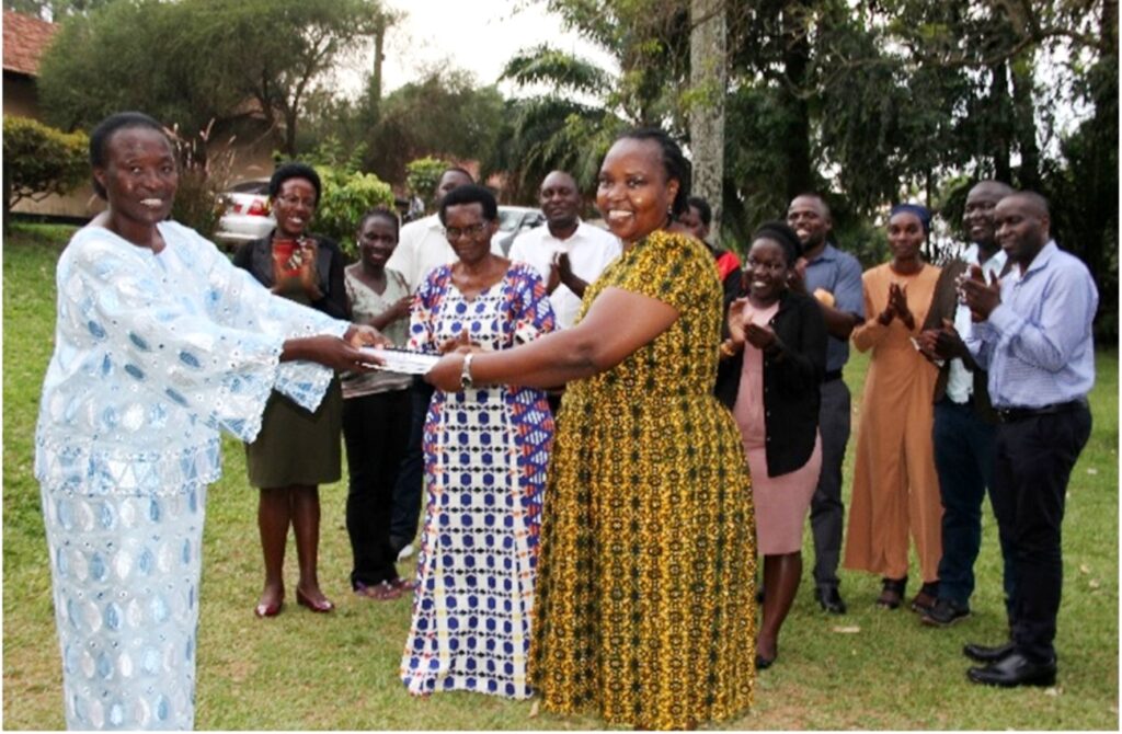 Ms. Frances Nyachwo handing over to Dr. Euzobia Mugisha-Baine as staff from the Directorate and Family members applaud