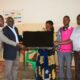 Dr. John Ssentongo and Mr. Stewart Mukiibi from the College of Education and External Studies (Left) hand over a Smart TV to officials of Lwamata Seed School in Kiboga District.