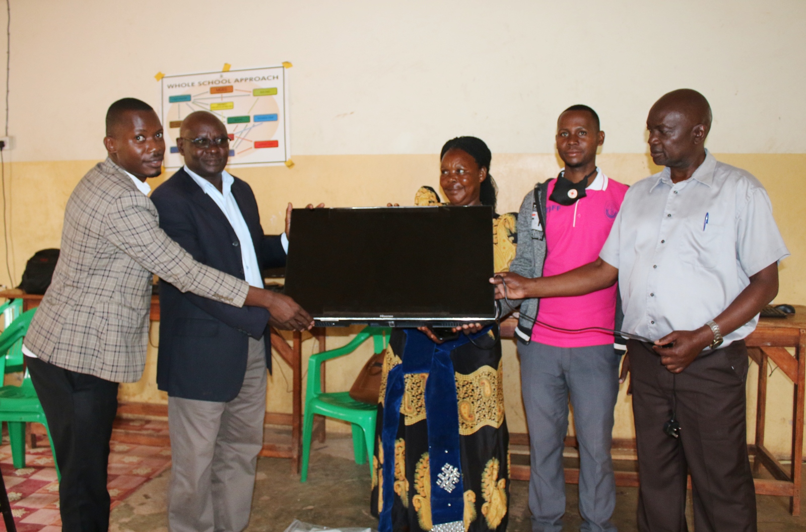 Dr. John Ssentongo and Mr. Stewart Mukiibi from the College of Education and External Studies (Left) hand over a Smart TV to officials of Lwamata Seed School in Kiboga District.