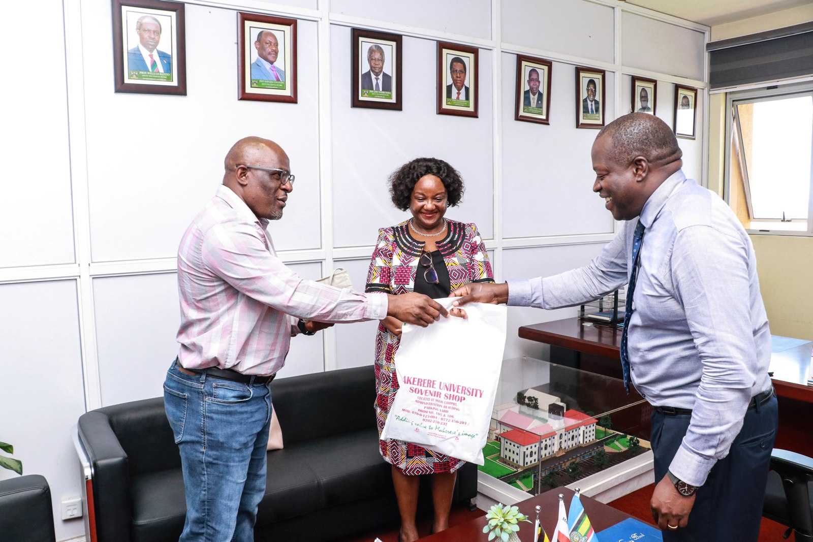 The Acting Deputy Vice Chancellor Finance & Administration, Prof. Tonny J. Oyana (R) presents an assortment of Makerere University souvenirs to BMGF's Dr. William Sambisa (L) during the courtesy call on 4th July 2022, Frank Kalimuzo Central Teaching Facility. Centre is the Dean MakSPH, Prof. Rhoda Wanyenze.