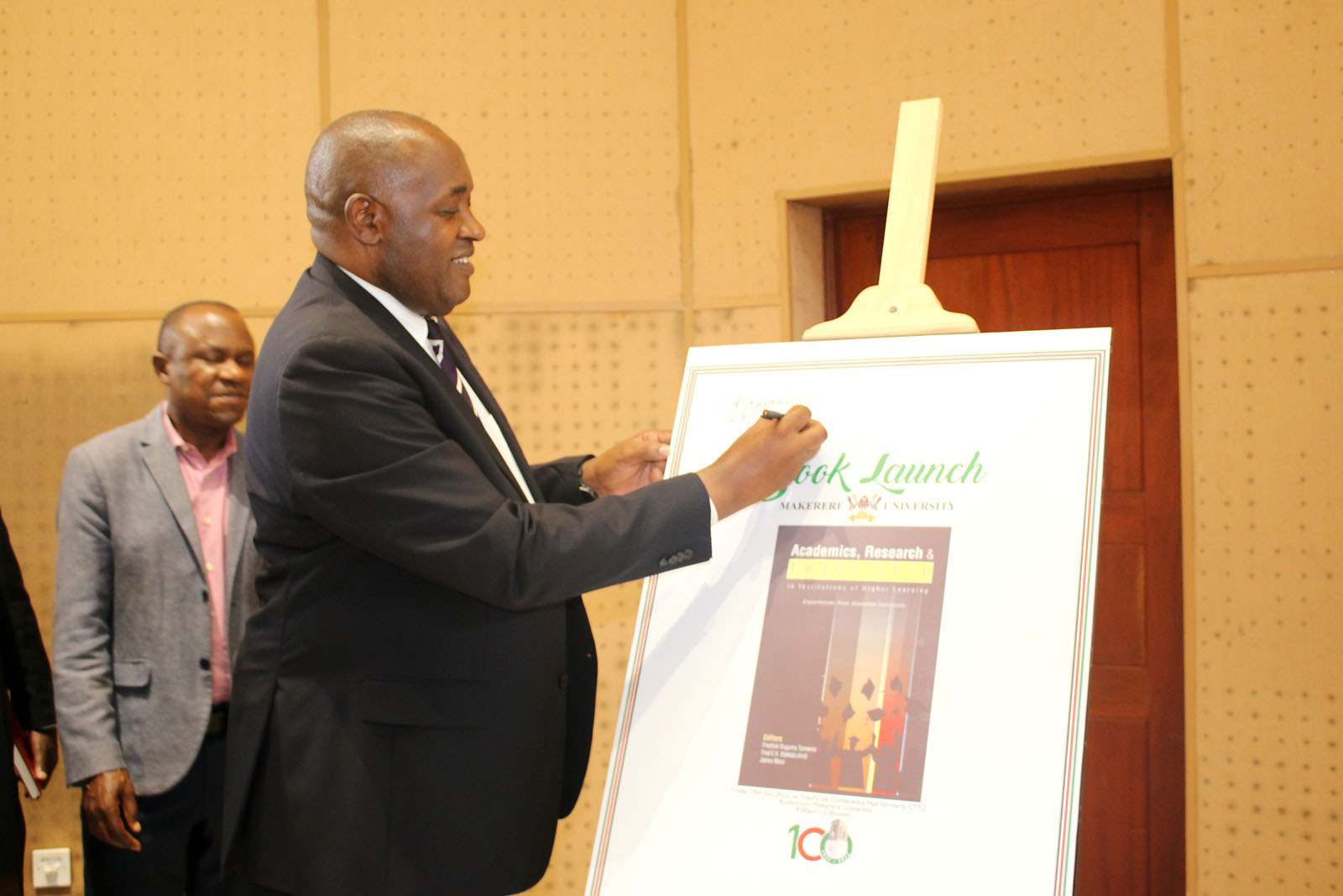 Hon. Chris Baryomunsi signs a dummy of the Book "Academics, Research and Leadership in Institutions of Higher Learning: Experiences from Makerere University" signifying its launch on 29th July 2022.
