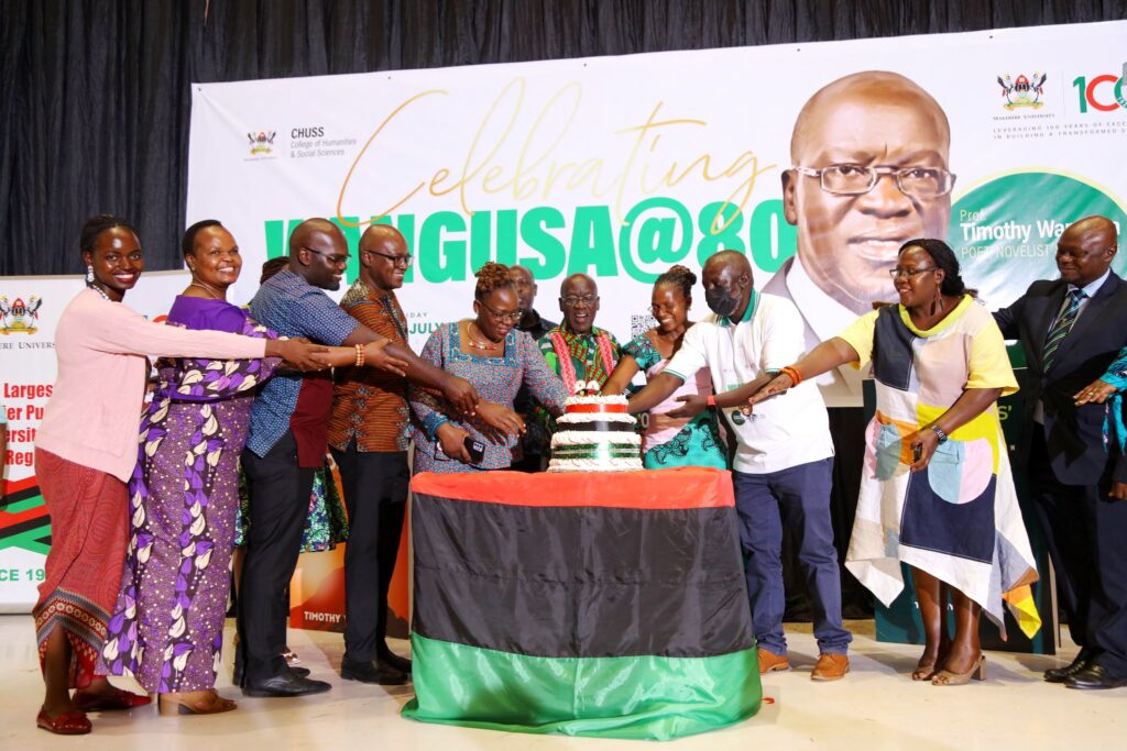 Professor Timothy Wangusa (5th R) is joined by family and CHUSS Leadership; Principal-Prof. Josephine Ahikire (2nd R), Deputy Principal-Dr. Eric Awich Ochen (R) and Head Literature-Dr. Edgar Nabutanyi (3rd R) to cut cake. 