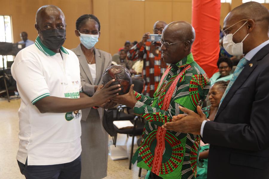 Dr. Edgar Nabutanyi (R) and Dr. Susan Kiguli (2nd R) present a gift to Professor Timothy Wangusa as the DVCAA, Professor Umar Kakumba applauds.