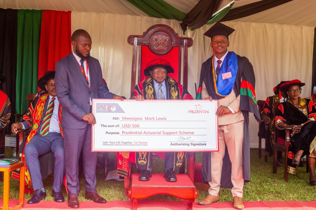 The Chancellor Prof. Ezra Suruma (C) witnesses as a Prudential Uganda representative presents a USD 500 dummy cheque to Mwesigwa Mark Lewis (R) who scored a CGPA of 4.00 in the Bachelor of Science in Actuarial Science. This was on Day 3 of the 73rd Graduation Ceremony of Makerere University held on 15th February 2023.