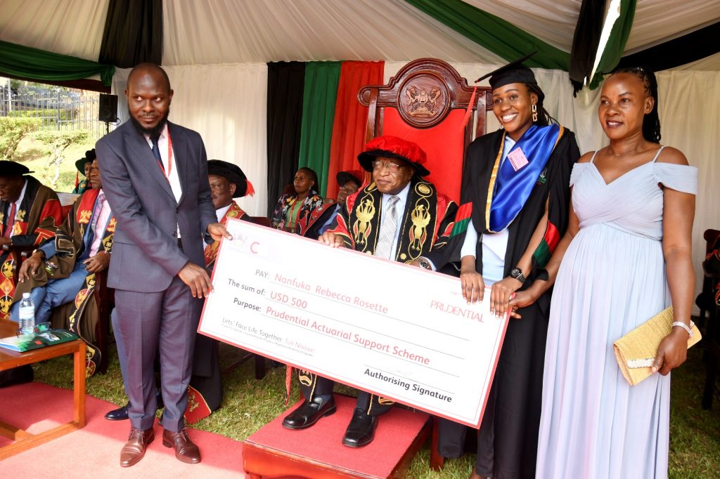 The Chancellor Prof. Ezra Suruma (2nd L) witnesses as a Prudential Uganda representative presents a USD 500 dummy cheque to Nanfuka Rebecca Rosette (2nd R) who scored a CGPA of 4.55 in the Bachelor of Science in Actuarial Science. This was on Day 3 of the 73rd Graduation Ceremony of Makerere University held on 15th February 2023.