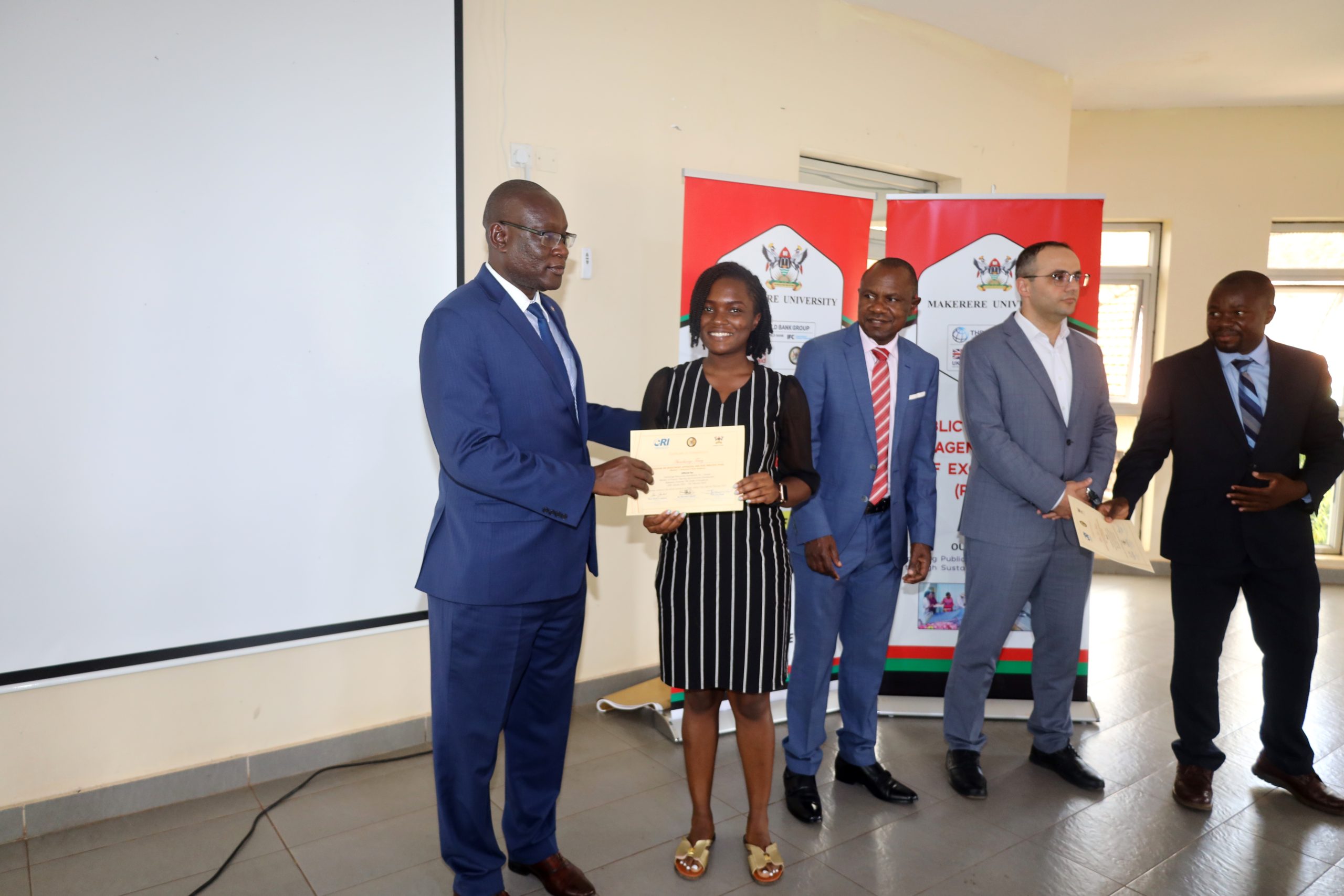 Mr. Ashaba Hannington (L), who represented the Permanent Secretary of MoFPED presents a certificate to one of the participants as the Principal CoBAMS, Prof. Eria Hisali (C), Dean of the School of Economics, Prof. Ibrahim Okumu (R) and another official witness on 10th February 2023.