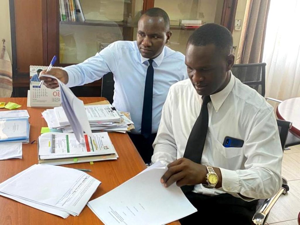 CHUSS HR Officer, Mr. Godfrey Makubuya (L) and a Representative from Internal Audit, Mr. Luwuliza Aggrey (R) browse through hand over documents in the Deans office.