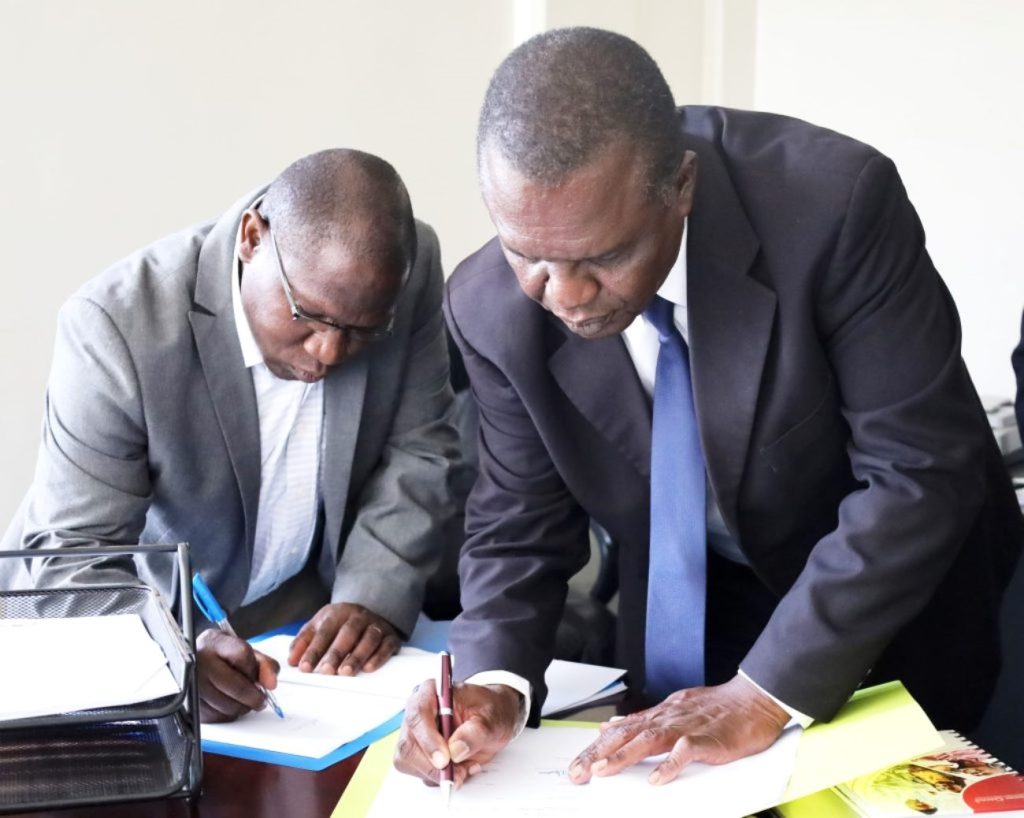 Dr. Joseph Balikuddembe and Assoc. Prof. Gilbert Mayiga sign the handover documents in the Dean's office.