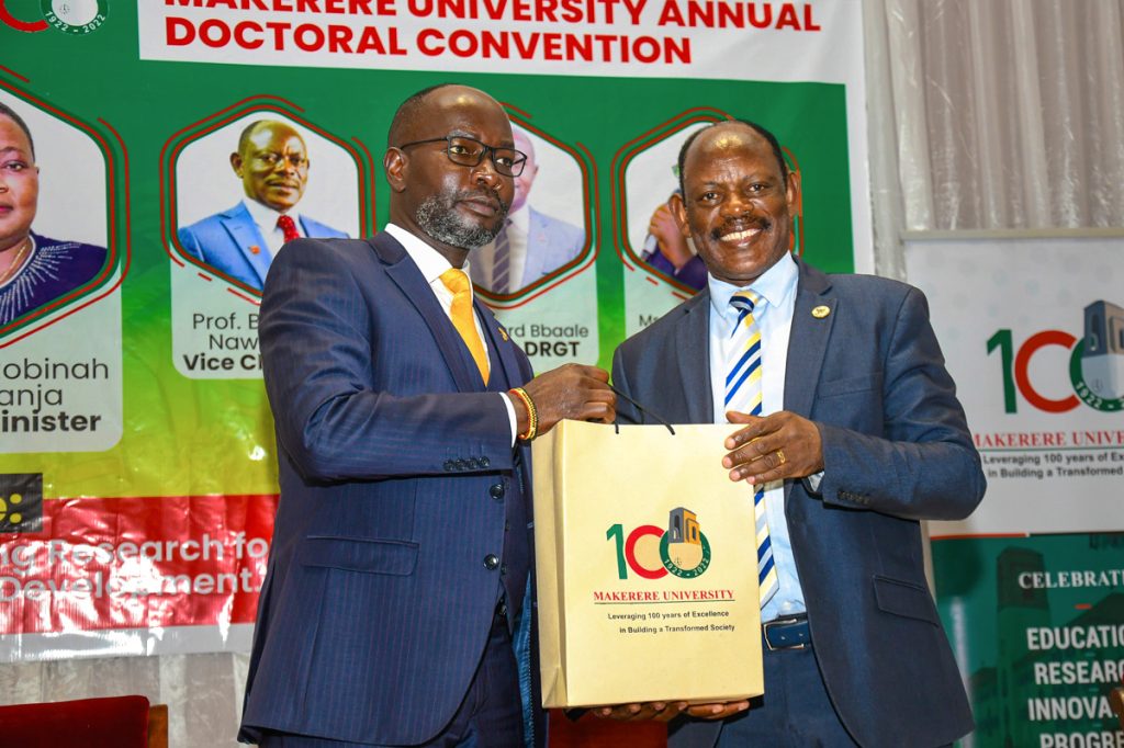 Hon. Denis Hamson Obua (L) receives an assortment of Mak Souvenirs on behalf of the Right Honourable Prime Minister from Prof. Barnabas Nawangwe (R) after delivering the Keynote address at the Makerere University Annual Doctoral Convention 2023.