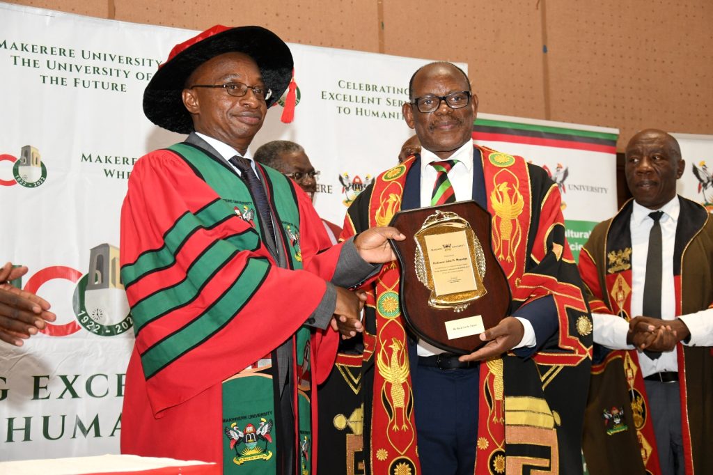The Vice Chancellor, Prof. Barnabas Nawangwe (Right) presents a plaque to Prof. John H. Muyonga (Left) as the DVCFA-Prof. Henry Alinaitwe (Rear Right) and other officials witness. Yusuf Lule Central Teaching Facility Auditorium, Makerere University, Kampala Uganda.