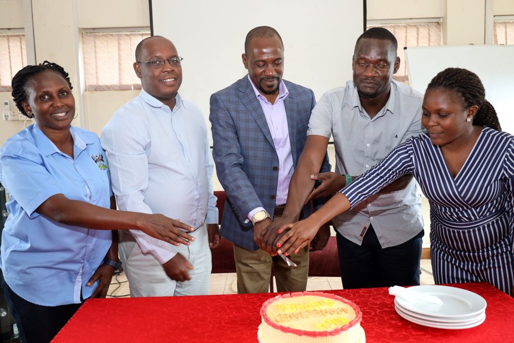 Mr. David Ikomo (2nd Right) and Mr. Stephen Byarugaba (Centre) are joined by Ms. Angida Franco Mugyema (Left), Dr. Peter Nabende (2nd Left) and another member of staff to cut cake. The Conference Room, Level 4, Block A, College of Computing and Information Sciences (CoCIS), Makerere University, Kampala Uganda, East Africa.