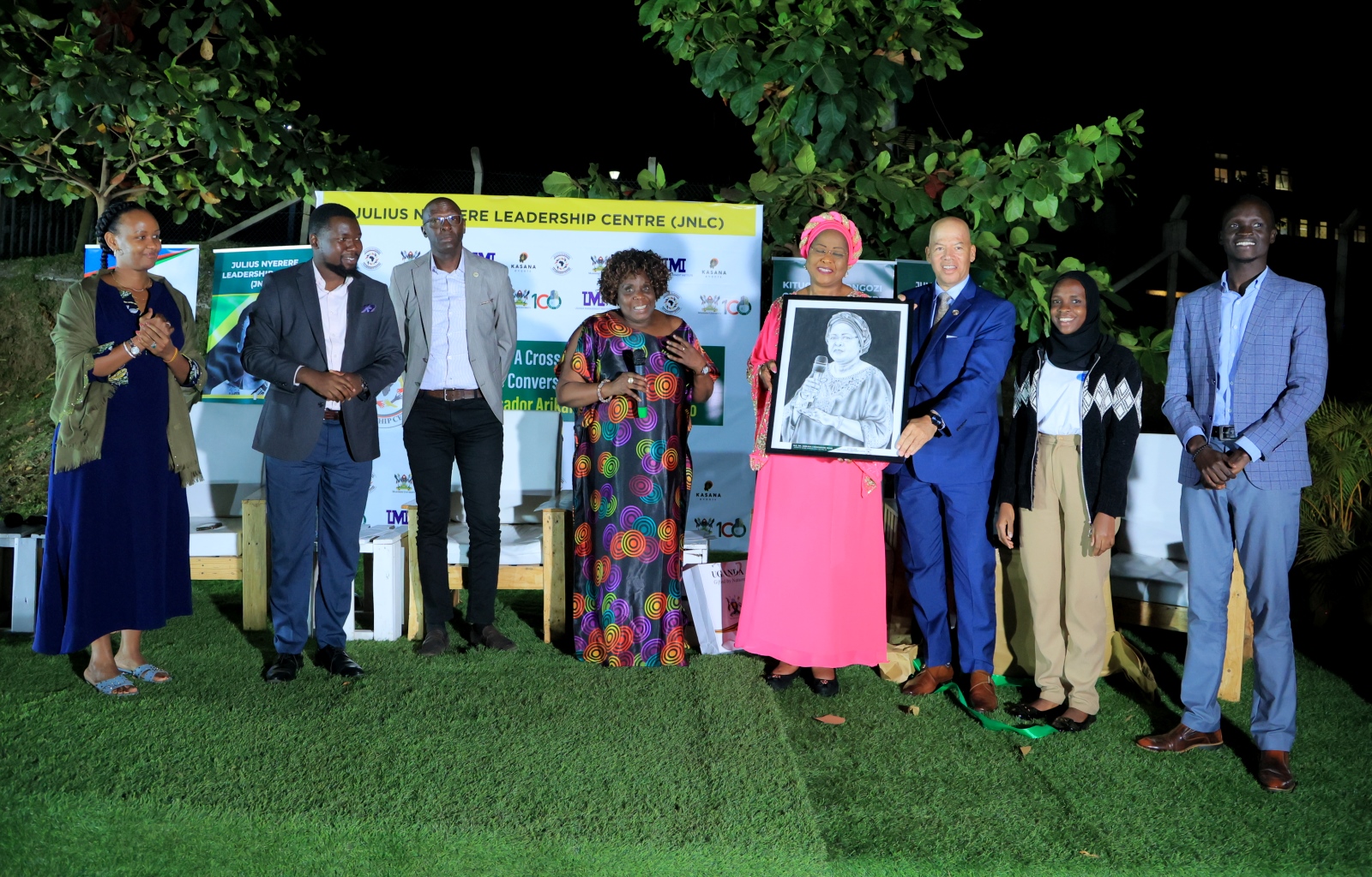 H.E. Amb. Dr. Arikana Chihombori-Quao (4th Right) shows off her portrait as Left to Right: Mrs. Esteri Akandwanaho Muhoozi, Mr. Jacob Eyeru, Mr. Andrew Tumusiime, Dr. Suzie Nansozi Muwanga, Mr. Damian Courtland Cook, H.E. Mariat Namiiro and Hon. Moses Jok Aluong witness at the Ekyooto on 26th July 2023, JNLC Gardens, Makerere University. Kampala Uganda, East Africa.