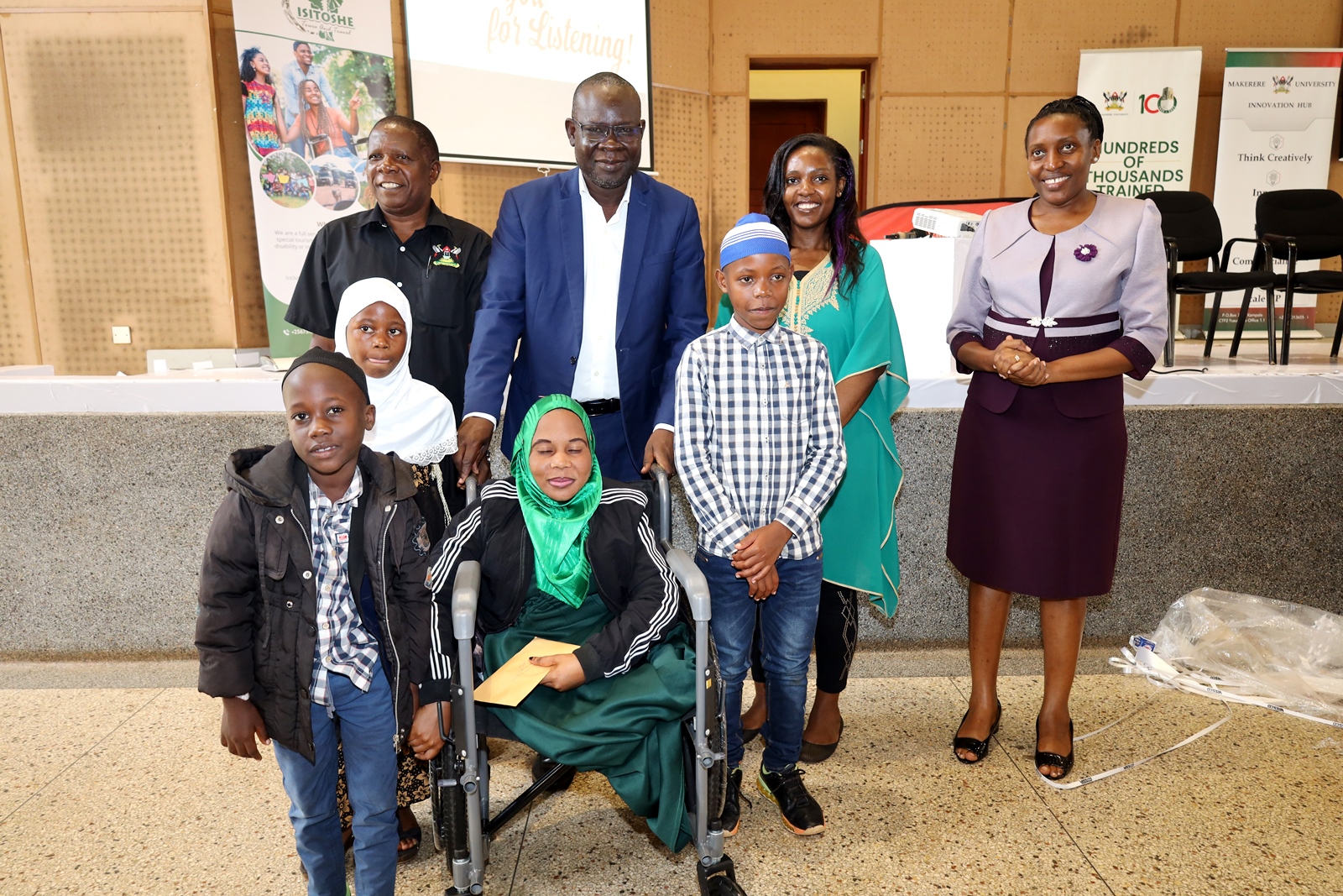 Standing: Dean School of Business-Prof. Godfrey Akileng (2nd Left), Head Department of Marketing and Management-Prof. Peter Turyakira (Left), Director, Makerere University Innovations Hub and Project PI-Dr. Cathy Mbidde (Right) with officials and some of the persons living with disabilities during the celebrations on 1st December 2023. Yusuf Lule Central Teaching Facility Auditorium, Makerere University, Kampala Uganda, East Africa.