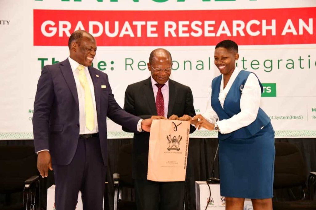 Hon. Dr. John C. Muyingo (Centre) receives an assortment of Makerere Souvenirs from Prof. Barnabas Nawangwe (Left) and Ms. Clare Cheromoi. Annual Forum for Graduate Research and Policy Dialogue, 25th April 2024, Yusuf Lule Central Teaching Facility Auditorium, Makerere University, Kampala Uganda, East Africa.