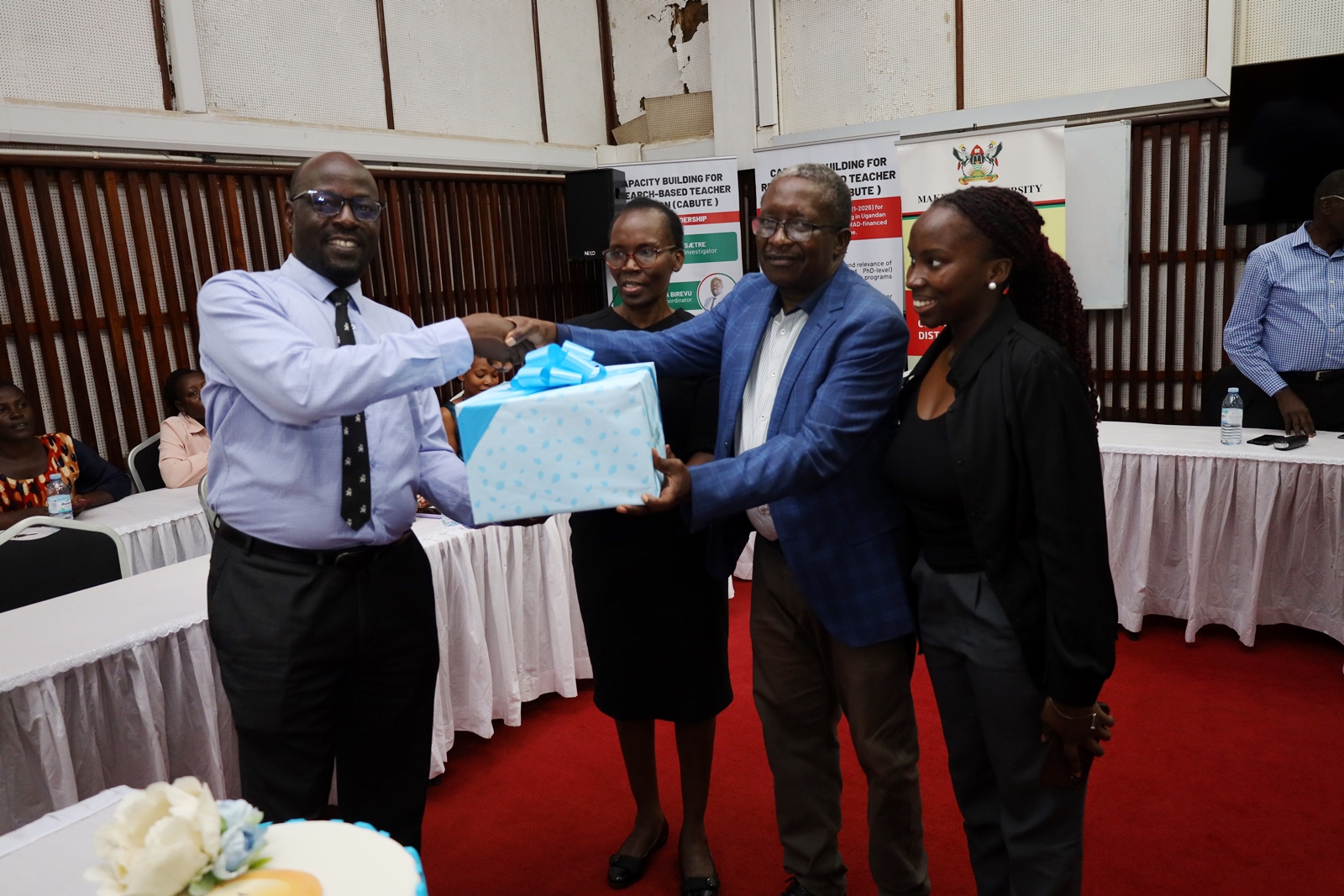 Dr. Samuel Siminyu (2nd Right) flanked by members of his family receives a gift from the Director IODeL, Prof. Paul Birevu Muyinda (Left) at the farewell event. Dr. Samuel Ndeda Siminyu farewell luncheon by the Institute of Open, Distance and e-Learning (IODeL) on 27th March 2024, AVU Conference Room, College of Education and External Studies (CEES), Makerere University, Kampala Uganda, East Africa.