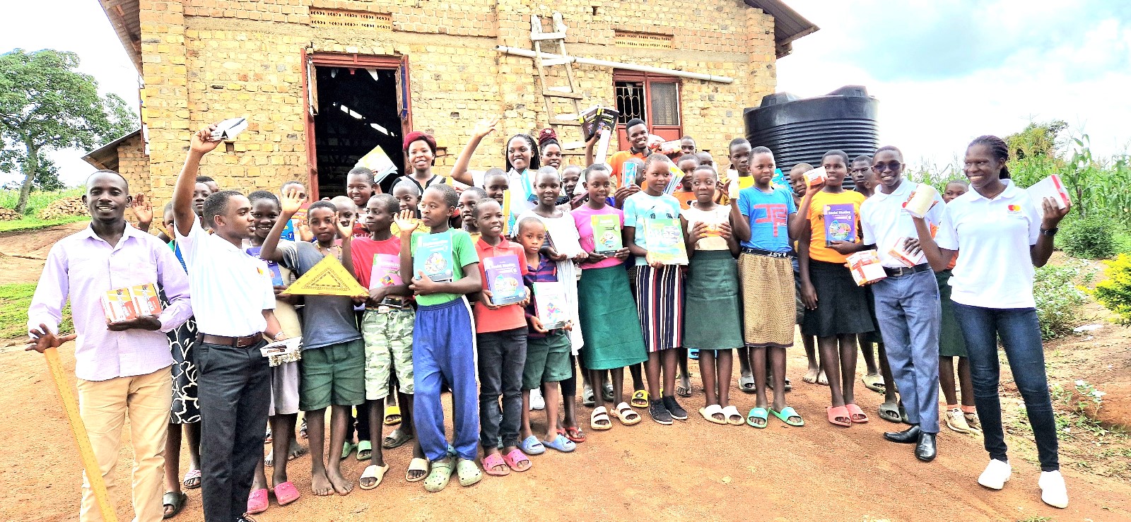 Mr. Alex Mugisha,the Headteacher, extreme left, pupils and staff of St. Charles Rwahunga Primary school very excited after receiving learning materials donated by Scholars of Mastercard Foundation. Mastercard Foundation Scholars at Makerere University, Kampala during the Annual Scholars Day of Community Service at Little Angels Nursery and Primary School in Ntenjeru, Mukono District, and St. Charles Rwahunga, Nursery and Primary School in Kyegegwa District, Uganda, East Africa, 16th November 2024.