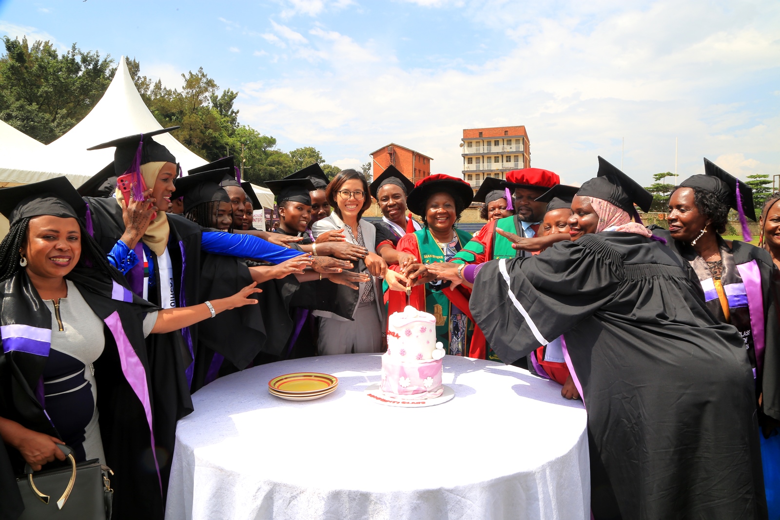 Ms. Elle Yang, Dr. Harriet Nabushawo and Dr. Jimmy Tibs Tumwesigye join some of the graduating candidates to cut cake. 240 students graduated with certificates and diplomas from the College of Education and External Studies (CEES) under the Love Binti Program, which offers training in fashion design and hairdressing, 13th December 2024, Impis Rugby Grounds, Makerere University, Kampala Uganda, East Africa.